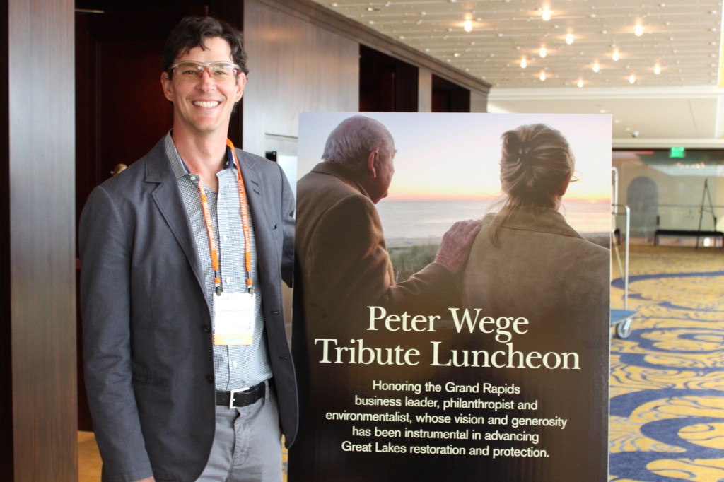 Andrew Goodwillie stands beside a photograph of his late grandfather Peter M. Wege and Terri McCarthy, Vice-President of programming for The Wege Foundation,  at the Healing Our Waters Conference's luncheon honoring Mr.  Wege. The accompanying   tribute video was shown at the luncheon.